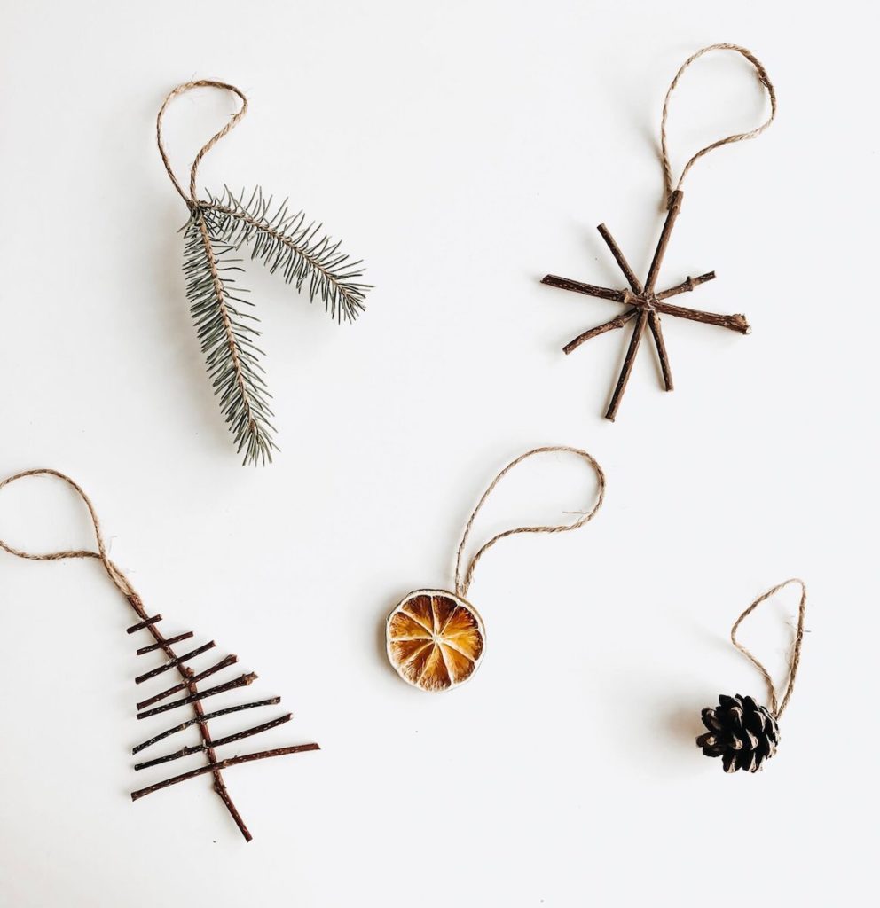 Flat lay photo of sustainable Christmas decorations on a white background including a dried orange and a snowflake made of sticks.