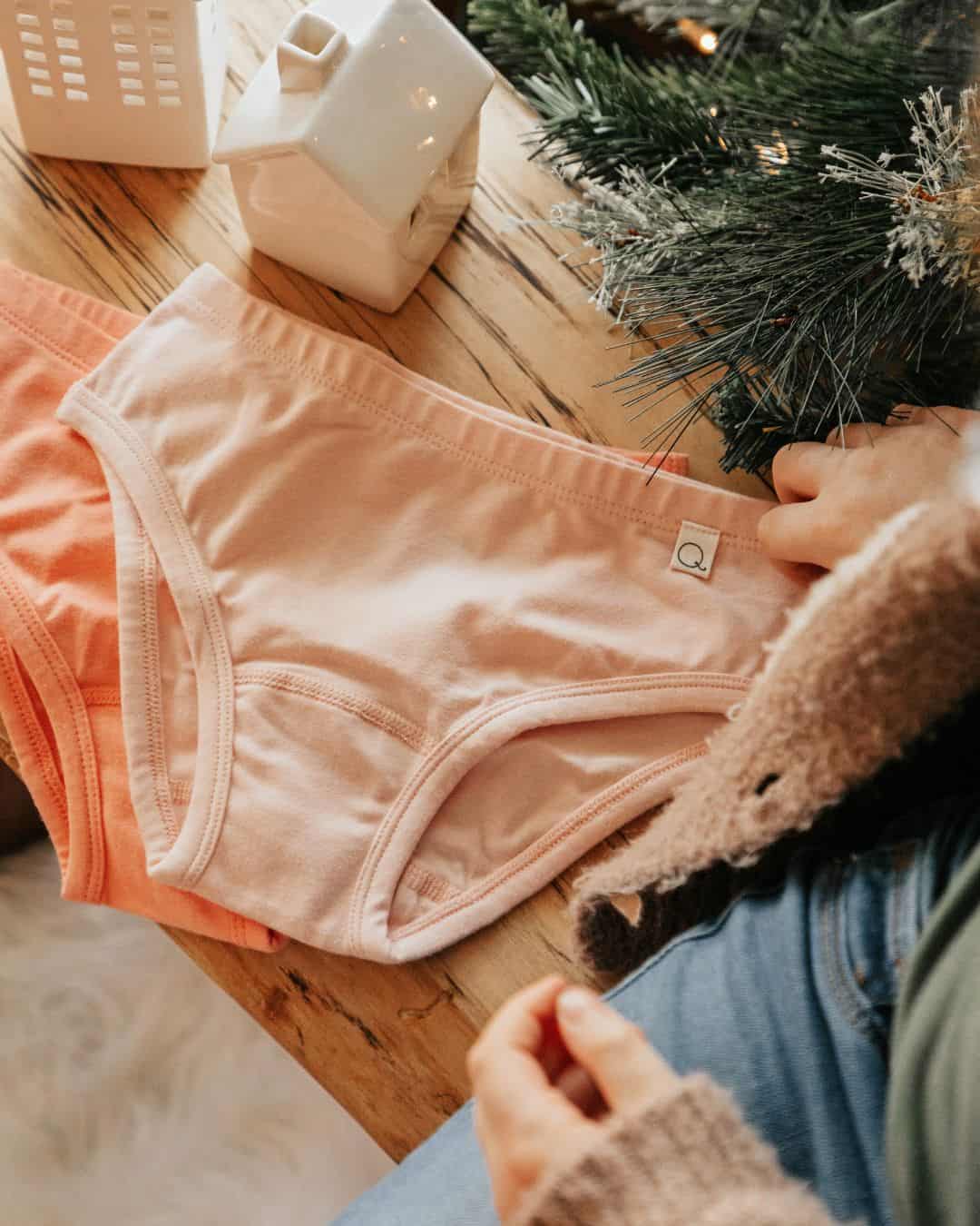 Pink organic cotton underwear laid on a wooden table beside holiday greenery for a guide to the best organic cotton underwear brands.