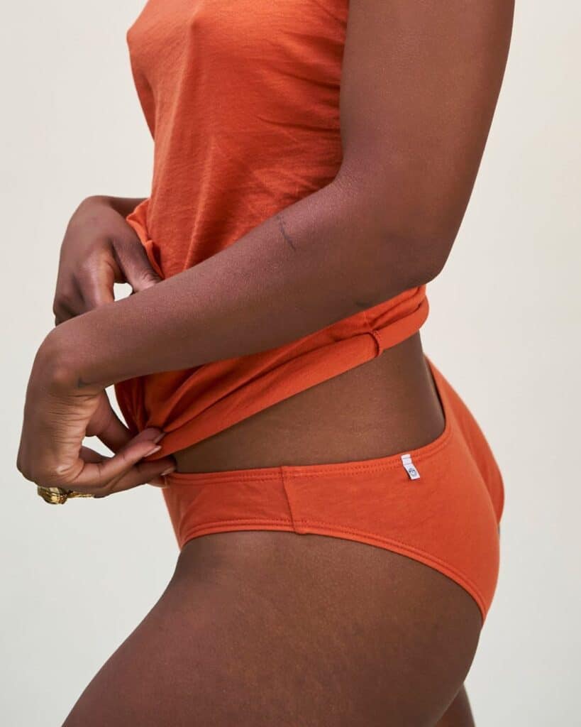 Model wearing rust-colored Oddobody organic cotton underwear with a matching cotton tank.