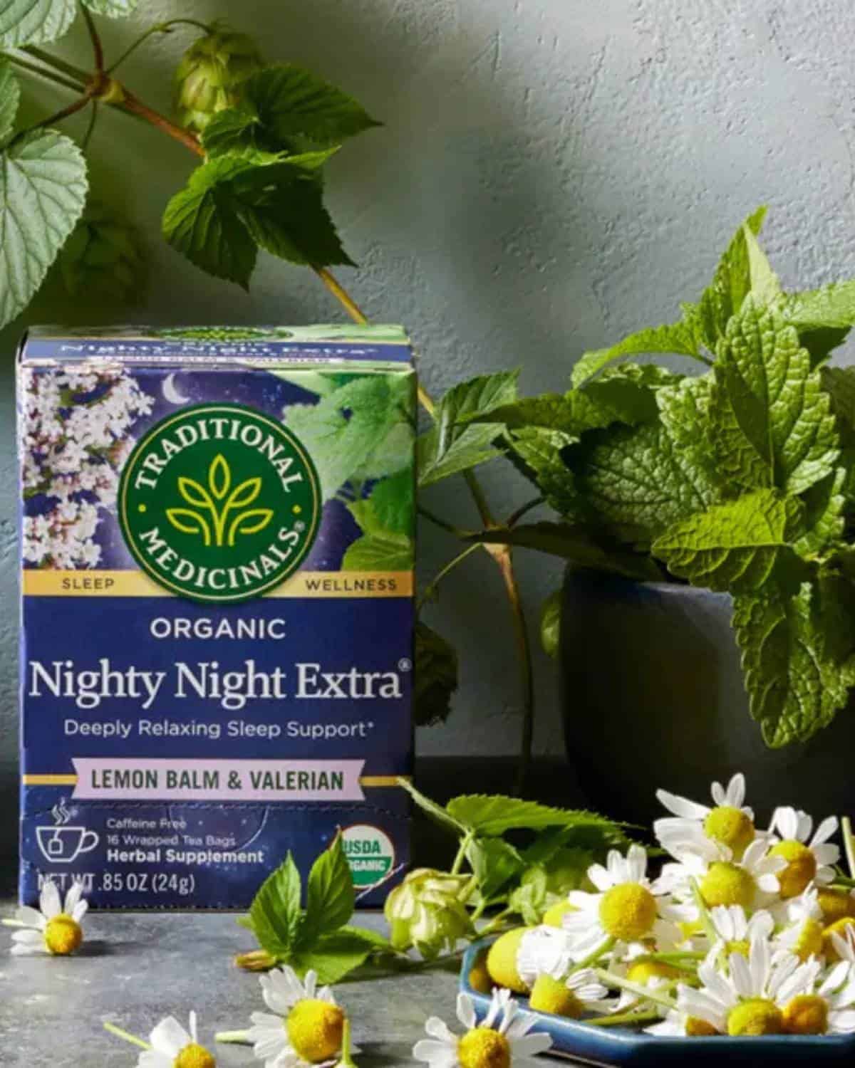 Box of Traditional Medicinals organic wellness tea next to a steeping mug and fresh herbs, illustrating their commitment to herbal remedies and verified purity.