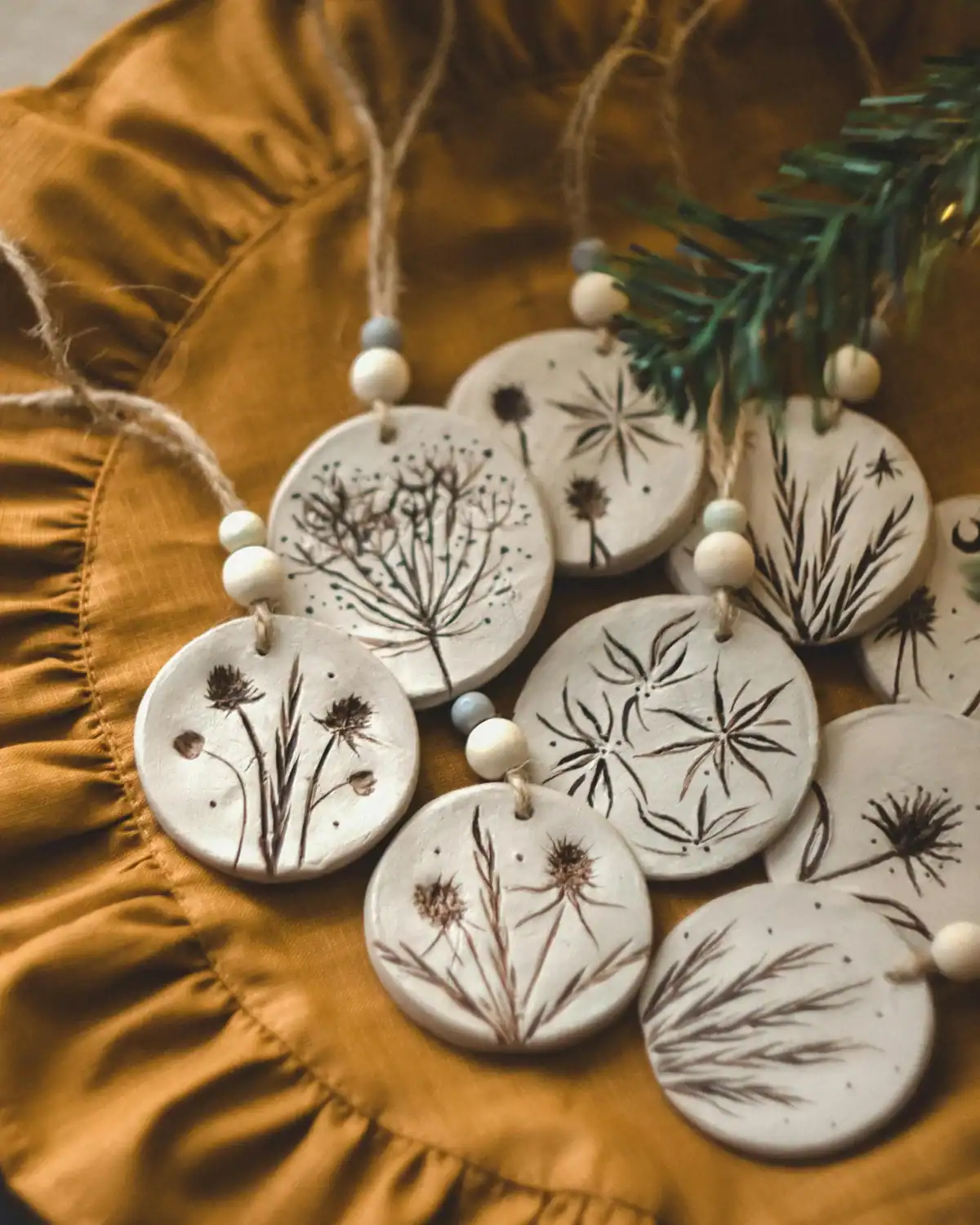 Handmade botanical air-dry clay ornaments with pressed and hand-drawn wildflower designs, twine, and wooden beads.