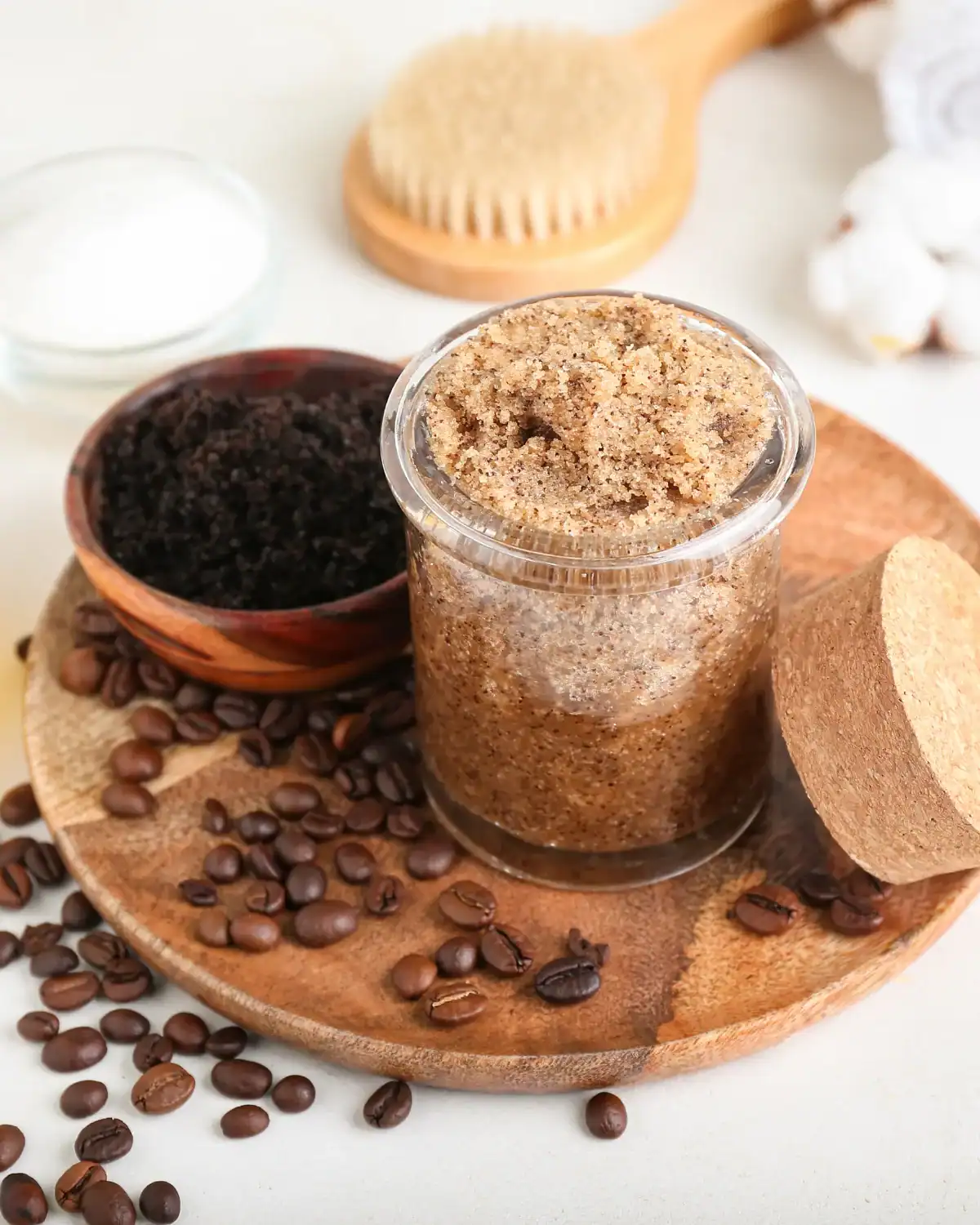 DIY brown sugar body scrub in a glass jar styled with coffee beans, coffee grounds, and a wooden body brush.