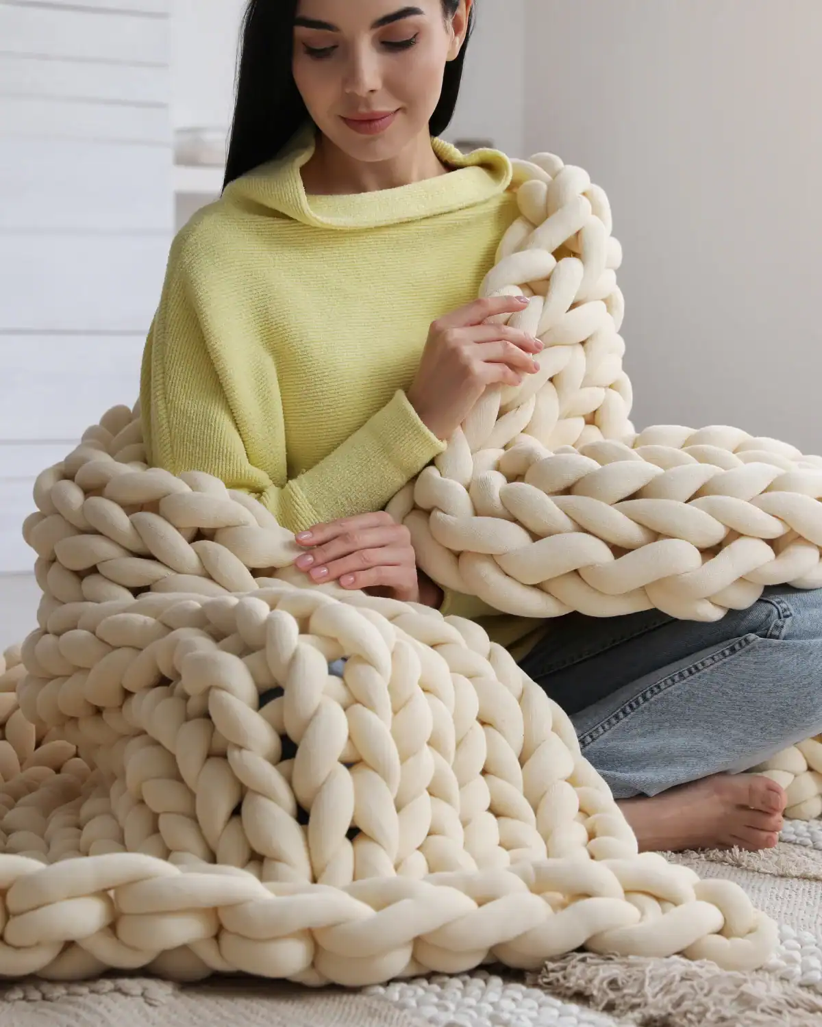 Woman wrapped in a cream chunky hand-knitted blanket made with oversized yarn.