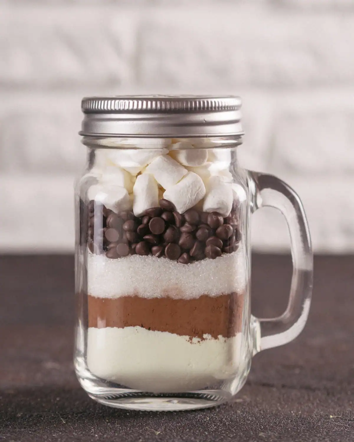 Layered hot cocoa mix in a mason jar with a ribbon and gift tag.