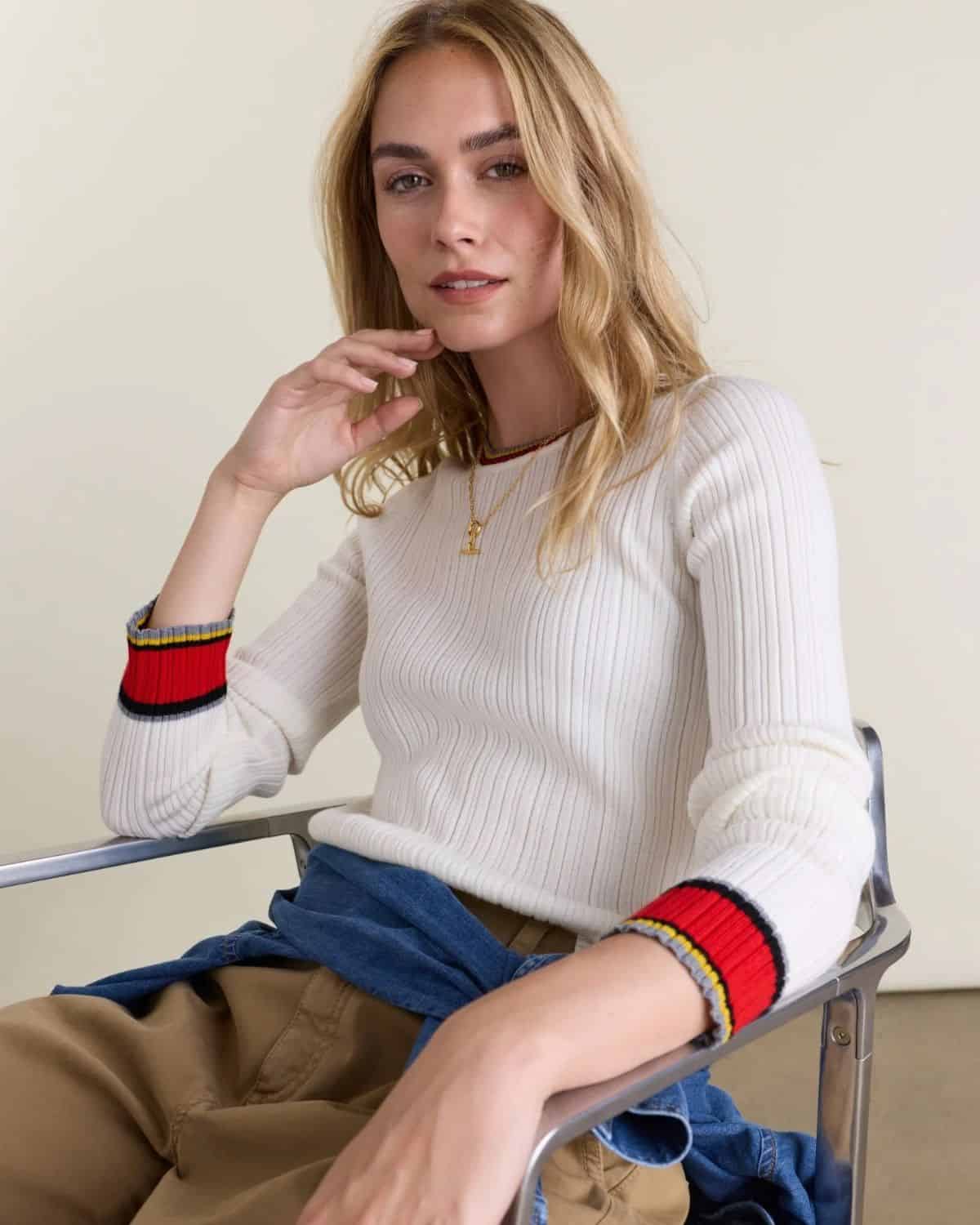 Woman wearing a white ribbed Baukjen organic cotton sweater with colorful striped cuffs, featured in a guide to non-toxic sweaters and cardigans