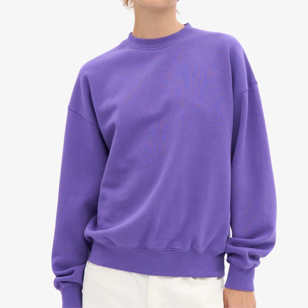 Woman wearing a purple crewneck sweatshirt featured as a bonus cozy layer in a guide to non-toxic sweaters and cardigans