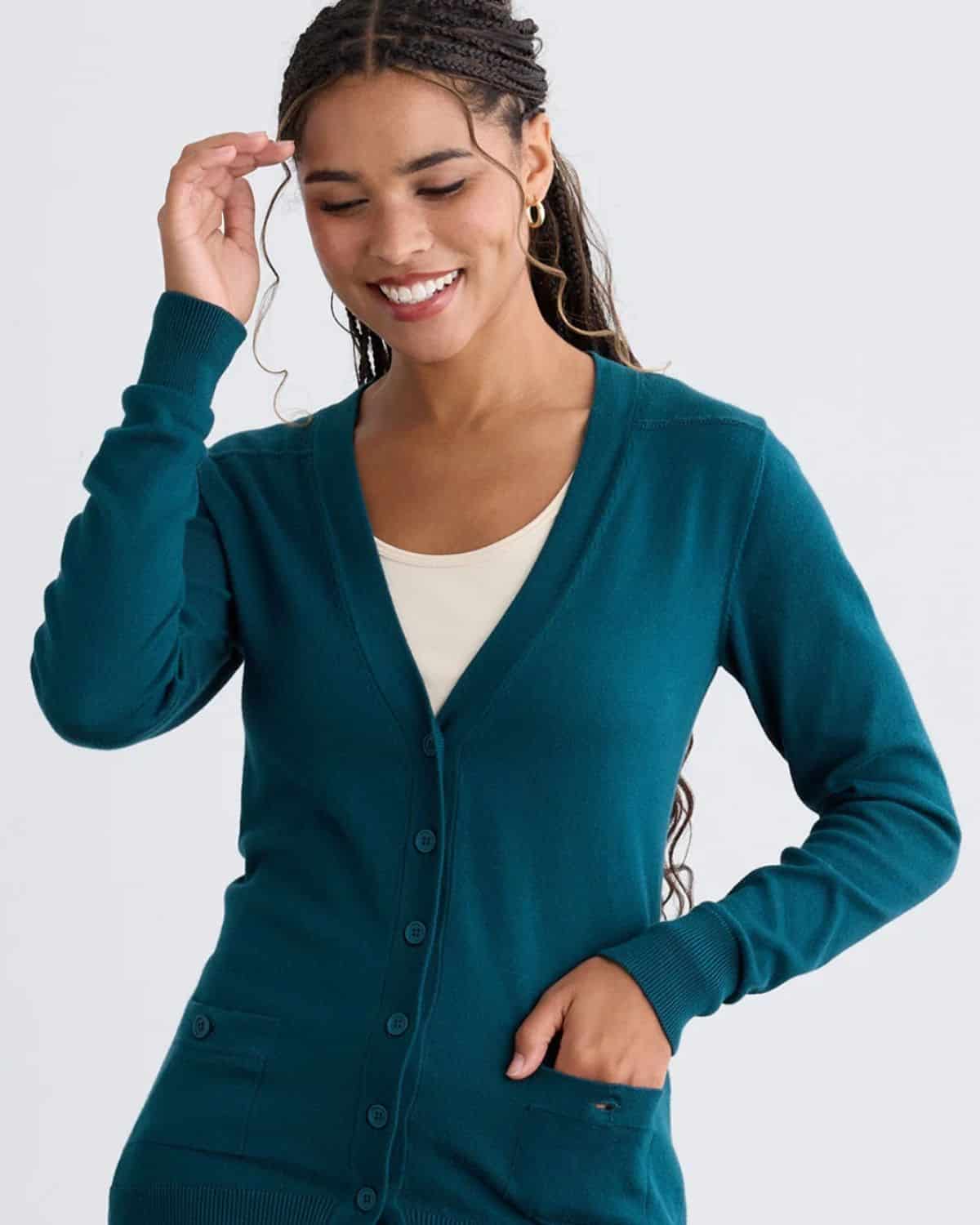 Woman wearing a teal Fair Indigo organic cotton V-neck cardigan with front buttons and patch pockets
