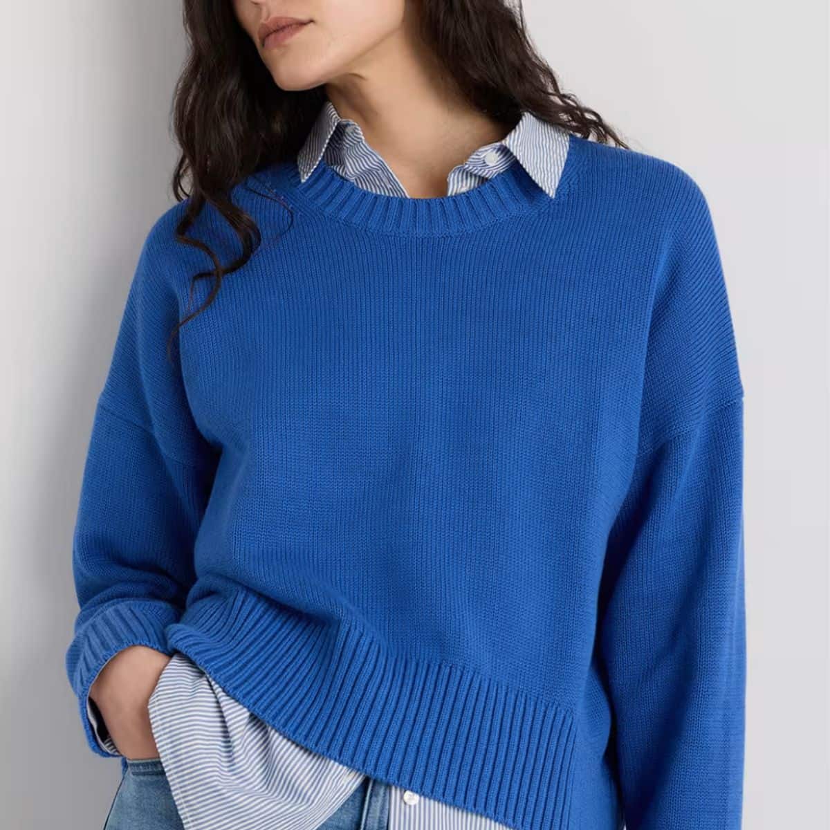 Woman wearing a bright blue Quince organic cotton crewneck sweater layered over a striped button-down shirt