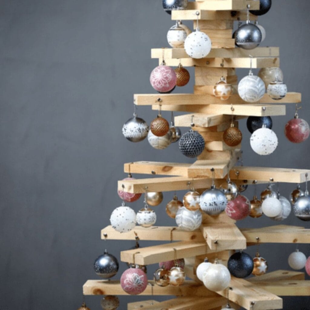Modern wooden Christmas tree made from stacked wood planks decorated with hanging Christmas ornaments.