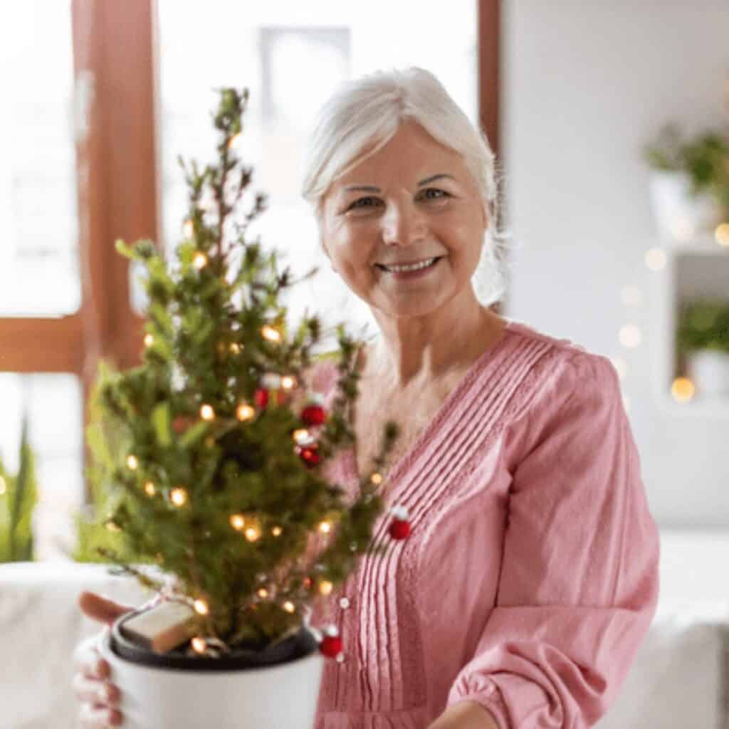 Small living evergreen Christmas tree in a glass vase decorated with gold ornaments as a sustainable holiday decoration.