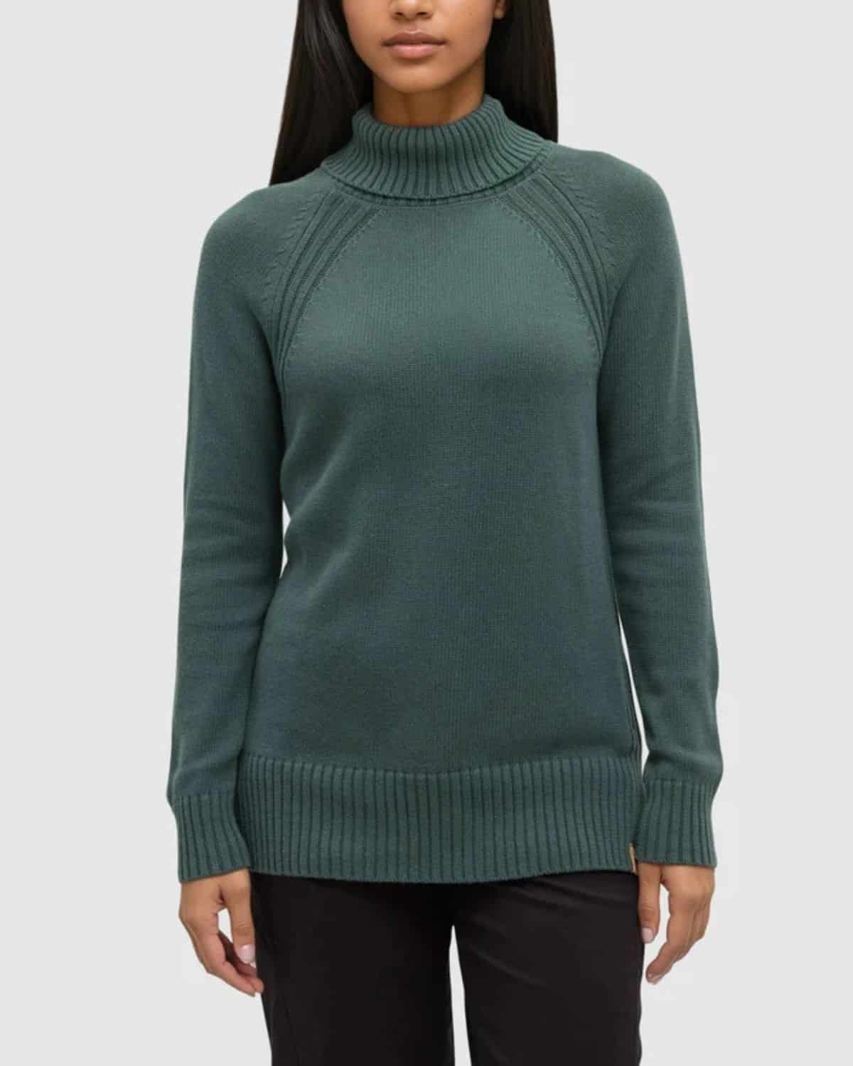 Woman wearing a forest green Tenure organic cotton turtleneck sweater with ribbed collar, cuffs, and hem