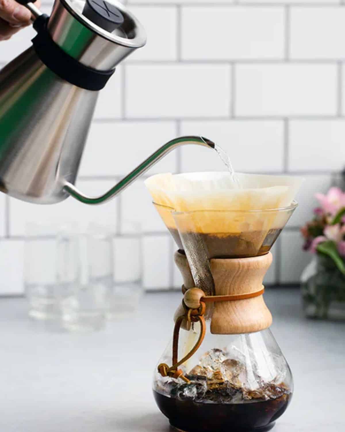 Hot water pouring from a gooseneck kettle into a paper filter in a Chemex glass pour-over coffee maker