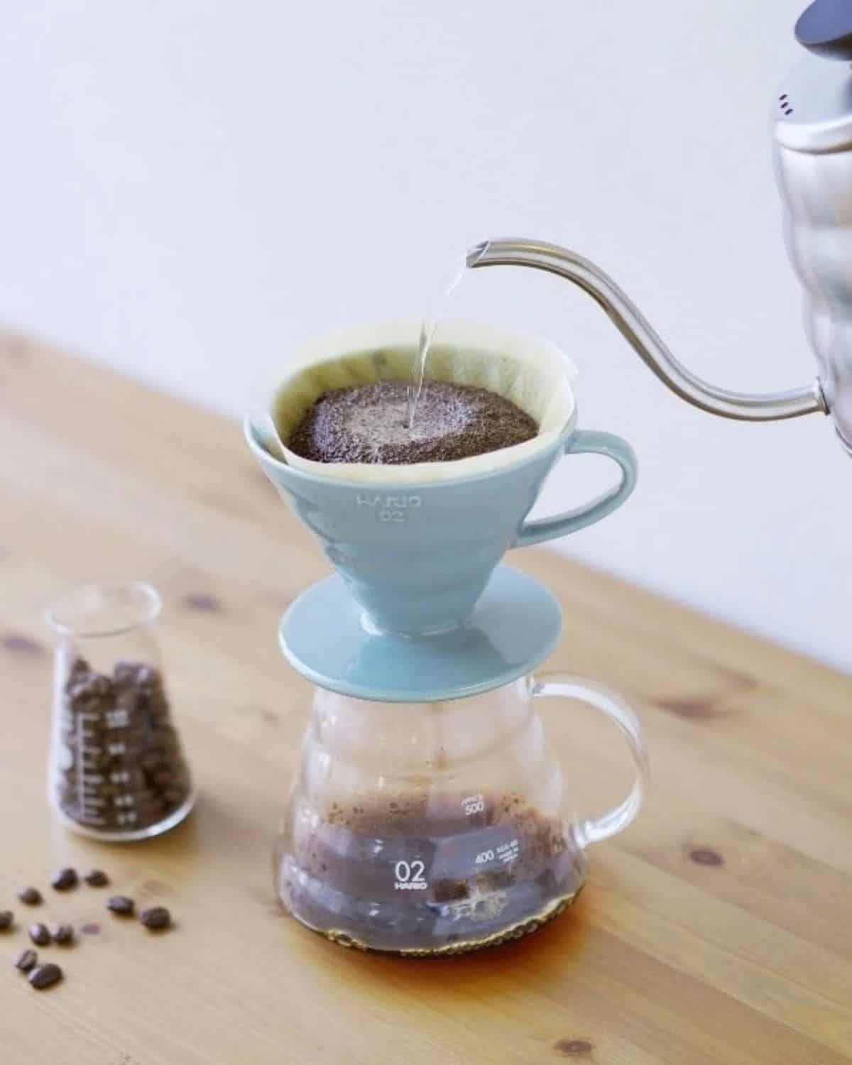 Hot water pouring into a blue Hario V60 ceramic coffee dripper over a glass server