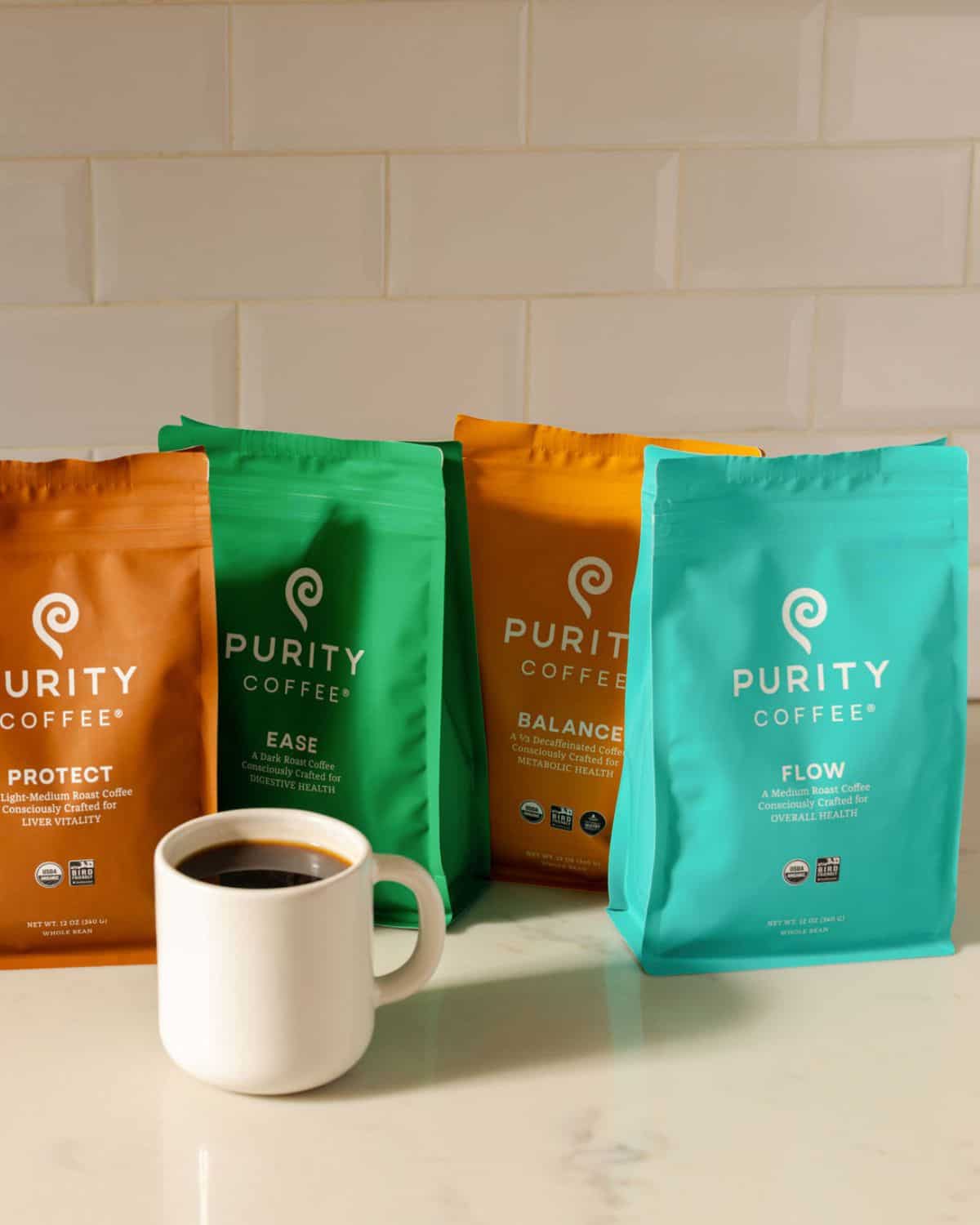Purity Coffee Protect, Ease, Balance, and FLOW organic whole-bean bags beside a white mug of black coffee.