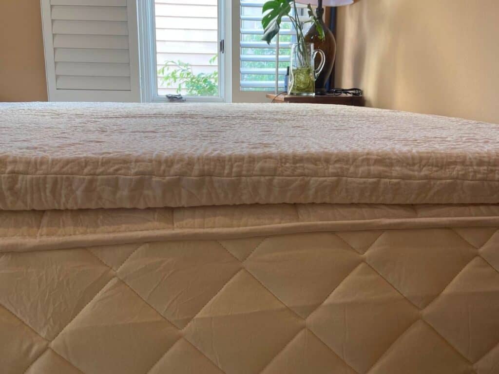 Side view of the Happsy organic mattress topper showing its thickness above the quilted King mattress.