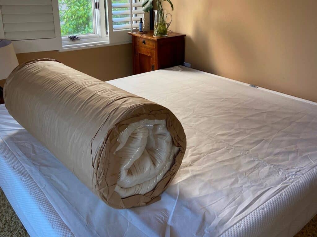 Compressed Happsy Plush King mattress rolled in protective packaging on the bed base during unboxing.