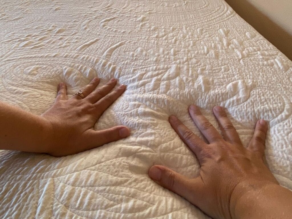Hands pressing into the Happsy organic mattress topper to assess cushioning during the Plush mattress review.